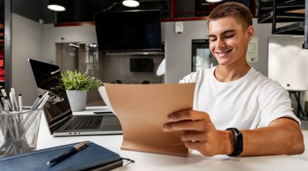 Young businessman making notes at tabletop with laptop in office close up